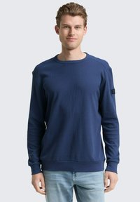 Dunkelblaue Langarm-Sweatshirt mit strukturiertem Stoff, Rundhalsausschnitt und gerippten Bündchen. Mit einem kleinen Logopatch am linken Ärmel.