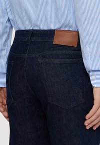 Vaqueros de mezclilla oscura con una textura suave, con una etiqueta de cuero en la cintura trasera que dice "TRUSSARDI" y bolsillos traseros estándar.