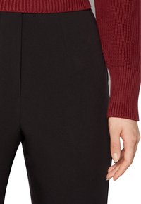 Burgundy knitted sweater with ribbed cuffs paired with black tailored pants. Focus on fabric texture and clean lines of the trousers.