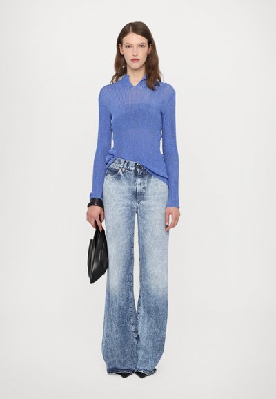 Blue ribbed knit top with a collar, paired with wide-leg light denim jeans. Model holds a black handbag. Clean, minimalist background.