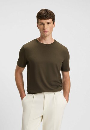 Olivengrøn, tekstureret kortærmet t-shirt med rund halsudskæring, parret med hvide, plisserede bukser. Enkel og moderne design.