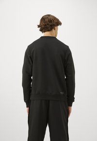 Sudadera negra con cuello redondo, puños y dobladillo acanalados. Presenta un logo sutil en la parte posterior, fabricada con una tela suave y texturizada.
