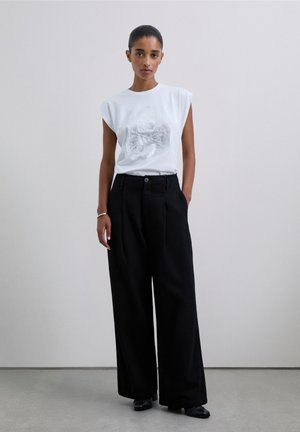 Camiseta blanca de manga corta con diseño gráfico combinada con pantalones negros de talle alto y pierna ancha. Tejido liso y ajuste holgado.