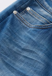 Tessuto in denim blu sbiadito con una leggera texture, caratterizzato da una tasca posteriore con bottoni metallici argento e cuciture marroni a contrasto.