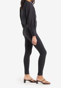 Jeans ajustados negros de cintura alta, hechos de mezclilla. Combinados con una blusa negra de mangas abullonadas y sandalias negras con tiras y tacón bajo.