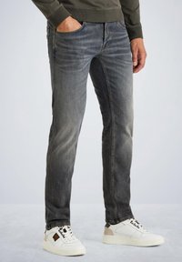 Jeans slim fit pour hommes en denim gris délavé avec une texture lisse, dotés de cinq poches et de détails subtils de décoloration, associés à des baskets blanches.