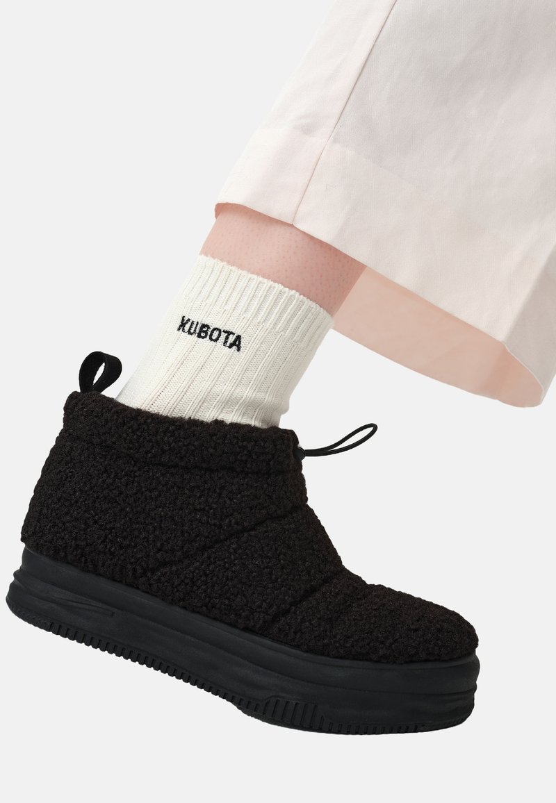 Czarne botki z polaru do kostki o teksturowanej powierzchni, z czarną gumową podeszwą i sznurowaniem do regulacji. W zestawieniu z białą skarpetą w prążki.