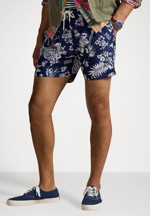 Marine zwemshorts met witte bloemen- en dierenprints, voorzien van een elastische waistbandsluiting met trekkoord. Gecombineerd met blauwe canvas sneakers.