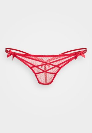 String rouge en dentelle avec un design à bretelles croisées, doté de fines bretelles et de nœuds de chaque côté, mettant en valeur une apparence délicate et texturée.