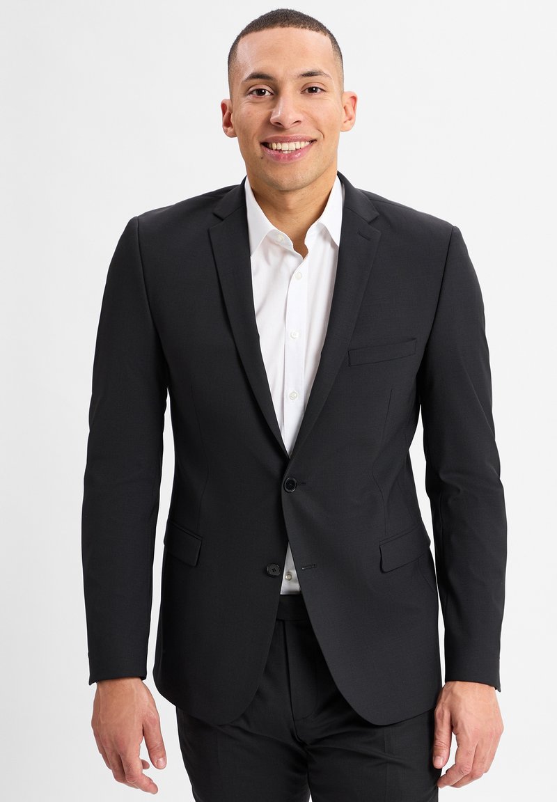 Zwarte blazer van gladde stof. Heeft een enkele knoop, notch-lapels en twee voorzakken. Draag het over een wit shirt.