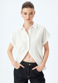 Maglietta bianca a maniche corte con colletto e tessuto strutturato, abbinata a jeans in denim scuri a vita alta; design con vestibilità rilassata.
