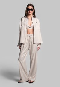 Lichtbeige gestreepte shirt, bijpassende cropped top en wijde broek. De stof heeft een gladde textuur. Accessoires zijn onder meer zwarte zonnebrillen.