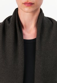 Sciarpa marrone scuro realizzata in tessuto morbido, drappeggiata in modo rilassato, con una texture liscia. Indossata sopra una maglietta nera a costine, che mette in risalto il décolleté.