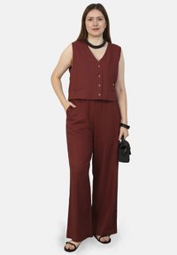 Bordeaux cropped vest met knopen, gecombineerd met wijde broek. Gelaagde stof, minimalistisch ontwerp en een kleine zwarte handtas. Platte sandalen.