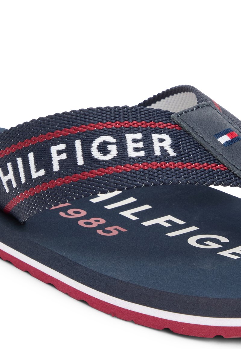 Chancla de playa Tommy Hilfiger en azul marino y rojo con tiras de tela texturizada, nombre de la marca en la tira y la plantilla, capas de suela en rojo y blanco.
