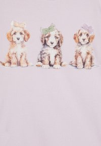 T-shirt di cotone con sfondo lilla che presenta tre cuccioli realistici, ciascuno con un fiocco di colore diverso sulla testa.