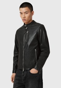 Veste de moto en cuir noir avec un col haut, fermeture éclair à l'avant et deux poches zippées. Texture lisse et design ajusté.