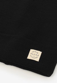 Zwarte gebreide beanie met een opgerolde rand en een rechthoekig stoffen label. Het label toont "DENIM BLEND with ATTITUDE" in een simpele lettertype.
