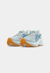 Light blue athletic shoes with a textured mesh upper and orange rubber sole. Featuring white laces and blue accents on the side.