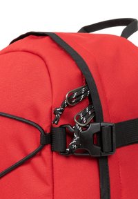 Sac à dos en tissu rouge avec une texture lisse, des bretelles noires et une boucle en plastique. Comprend des accents en cordon élastique pour une utilité accrue.