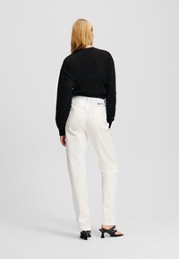 Felpa nera corta, jeans bianchi a vita alta e sandali neri con tacco. Vestibilità su misura, cuciture visibili e dettagli con logo sui jeans.