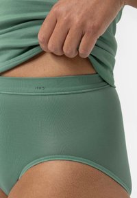 Groene katoenmix ondergoed met een gladde textuur en een elastische tailleband, gedeeltelijk bedekt door een loszittend shirt.