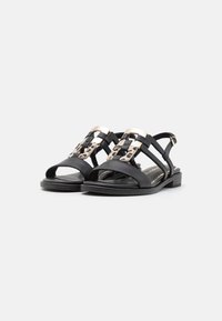 Black sandals with open toe design, woven straps, and gold-tone hardware featuring a leopard print accent in the center. Low, solid heel.