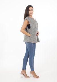 Szary kamizelka z sztucznego futra o bezrękawnikowym fasonie, z bocznymi kieszeniami i luźnym krojem, w połączeniu z jasnoniebieskimi dżinsami i przezroczystymi sandałami na obcasie.