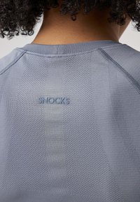 Maglietta sportiva grigia in tessuto strutturato, con motivi a maglia e rete. Logo "SNOCKS" impresso sulla parte alta della schiena. Design semplice con collo a giro.