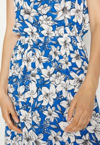 Vestido floral com um fundo azul e grandes padrões de lírios brancos e pretos. Tecido leve, cintura elástica e corte descontraído.