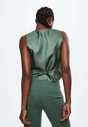 Groene satijnen mouwloze top met een gestrikt detail op de rug, gecombineerd met bijpassende groene getailleerde broek met ribbelstructuur en zijzakken.