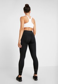Leggings neri con vita alta e dettagli riflettenti, abbinati a un reggiseno sportivo bianco con design racerback.