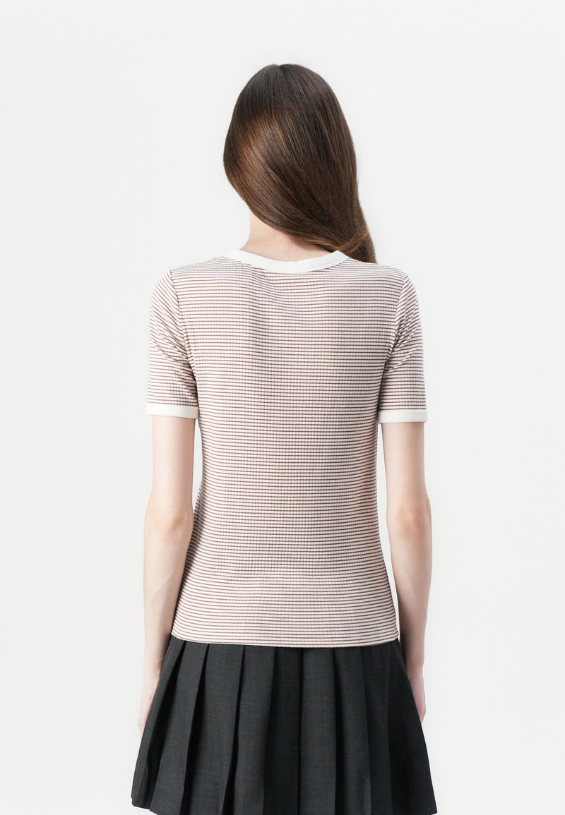 Krótki rękaw, prążkowany top w jasnoróżowym kolorze z ciemnymi paskami oraz białym okrągłym dekoltem. Połączony z czarną plisowaną spódnicą.