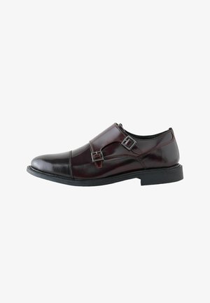 Dunkelbrauner Herrenschuh aus Leder mit doppelten Monk-Riemen und schwarzer Sohle, seitlich auf weißem Hintergrund gezeigt.