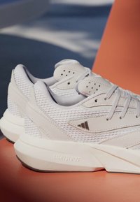 Baskets blanches en mesh et cuir avec semelles épaisses Lightstrike posées sur une surface orange, montrant les détails latéraux et arrière.