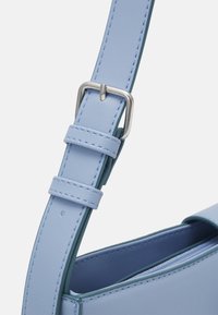 Sangle de sac à main synthétique bleu clair avec une boucle en métal argenté, présentant des coutures bleues supplémentaires et une texture lisse.