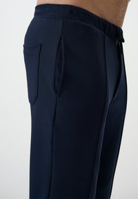 Navyblauwe sportbroek van gladde stof, met een elastische tailleband, koordje en twee zijzakken met minimale stiksels.