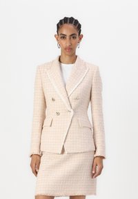 Blazer de tweed rosa claro com um design de duplo peito, botões grandes e lapelas recortadas; combinado com uma saia correspondente. Acabamento texturizado.