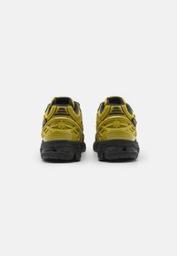 Gule og svarte joggesko med en teksturert gummisåle, som har et støttende design, avrundet hæl og pustende overdel.