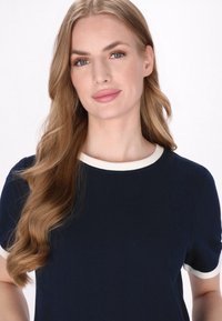 Marineblauwe t-shirt met korte mouwen en een crèmekleurige ronde hals. Glad stofstructuur, aansluitend ontwerp met contrasterende accenten op de mouwen.