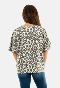 Camiseta de leopardo en gris y blanco con mangas cortas y sueltas, escote redondo y textura suave, combinada con jeans azules.