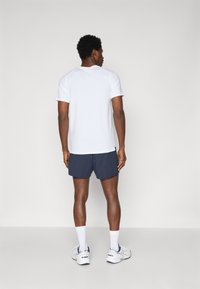 Hvit kortermet trenings t-skjorte kombinert med mørk marineblå shorts, iført hvite sokker og treningssko, med en jevn tekstur og praktisk passform.