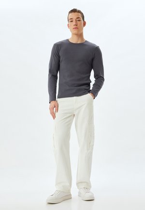 Grijze geribbelde blouse met lange mouwen, gecombineerd met witte cargobroeken met zijzakken en een relaxte fit, afgemaakt met witte sneakers.