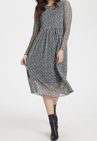 Vestido de manga larga con estampado floral en azul marino con pequeñas flores amarillas y blancas. Tela ligera y transparente, cintura fruncida, falda fluida, combinado con botas negras.