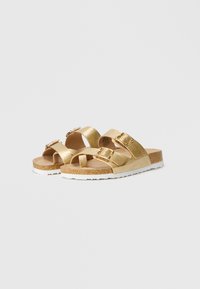 Χρυσές μεταλλικές σαγιονάρες με δύο ρυθμιζόμενες λουρίδες, φελλό στο πάτο, και λευκή καουτσούκ σόλα. Ικανός σχεδιασμός κατάλληλος για καθημερινή χρήση.