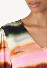 Bluza z dekoltem v v lahkem materialu z večbarvnim dizajnom, ki vključuje vodoravne črte v zeleni, roza, oranžni in bež barvi.