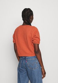 Avklippt orange stickad tröja med puffärmar, kombinerad med högmidjade blå denimjeans med detaljer på bakfickorna.
