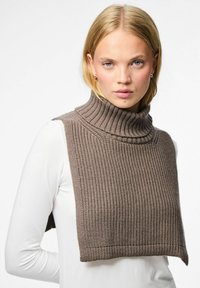 Ruskea neulottu kauluspaidalla, jossa on teksturoitu, ribattu kuvio. Hihaton malli kerrostettuna valkoisen pitkähihaisen paidan päälle.