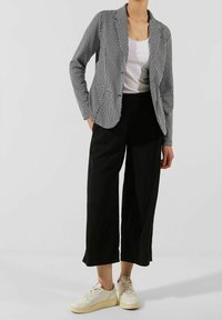 Blazer pied-de-poule noir et blanc porté sur un haut blanc, associé à un pantalon noir à jambes larges et des baskets crème. Design ajusté avec col à revers.