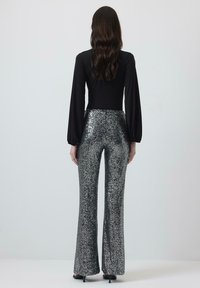 Zwarte lange mouwen bodysuit gecombineerd met glanzende, pailletten zilveren flared broek. Zachte textuur met een reflecterende oppervlakte en een getailleerde taille.